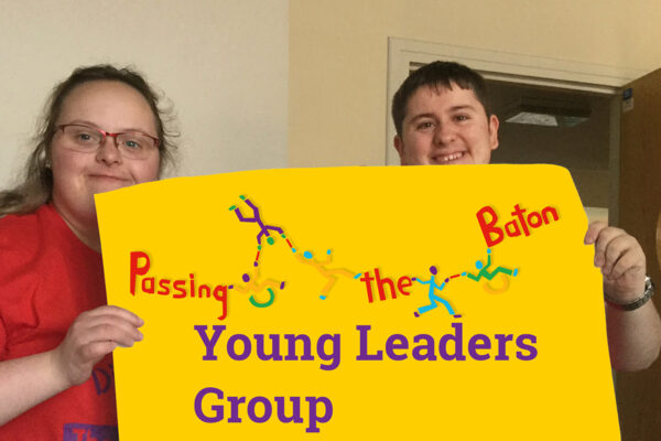 Photo of 2 of DIY's young leaders holding up a piece of paper with Passing the Baton logo and "Young Leaders Group"