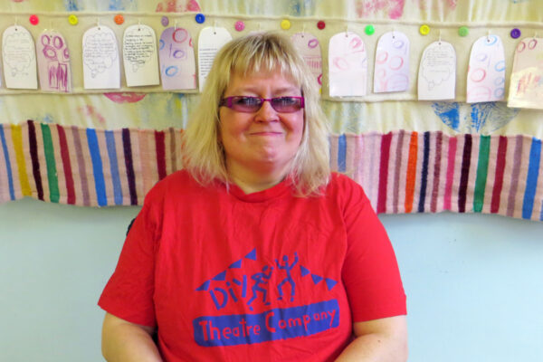 photo of Ange, she is wearing glasses and looks like she is holding in a laugh! She is sitting in her wheelchair and wearing a red DIY t-shirt