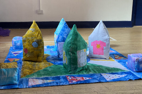 the close knit soft handling textile sculptures are conical shaped in yellow, blue, green and white, they are placed on a colourful textile play board / quilt